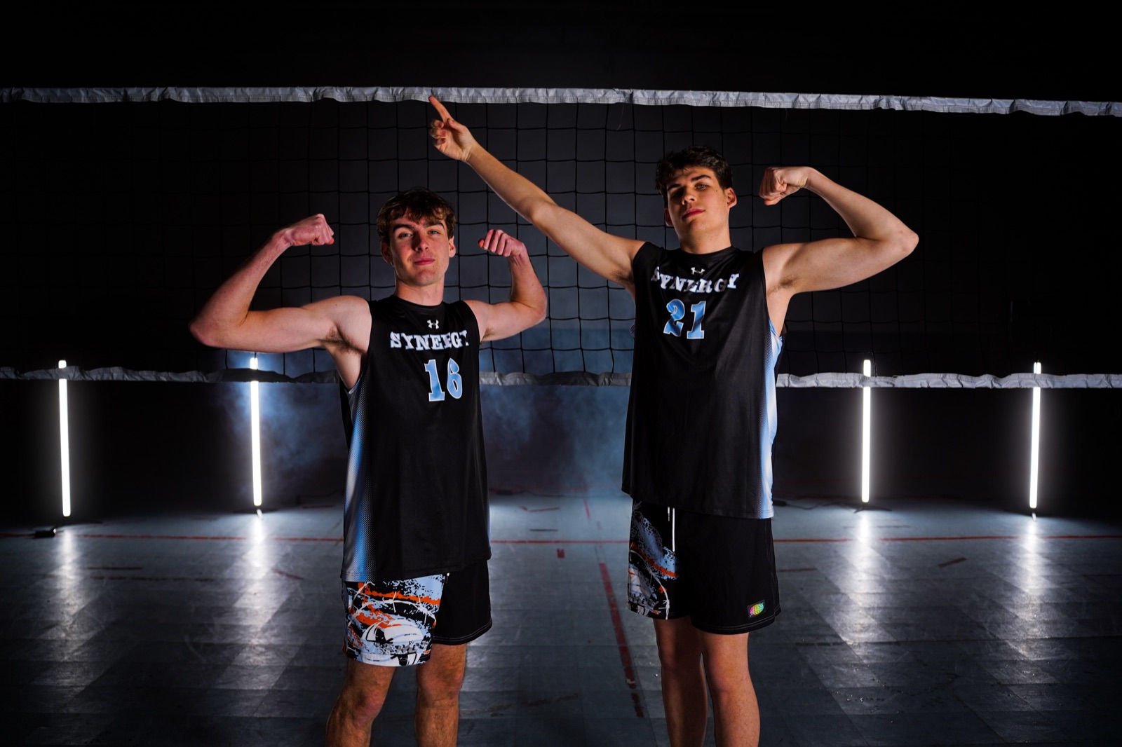 Two teammates flexing back-to-back under cool lighting