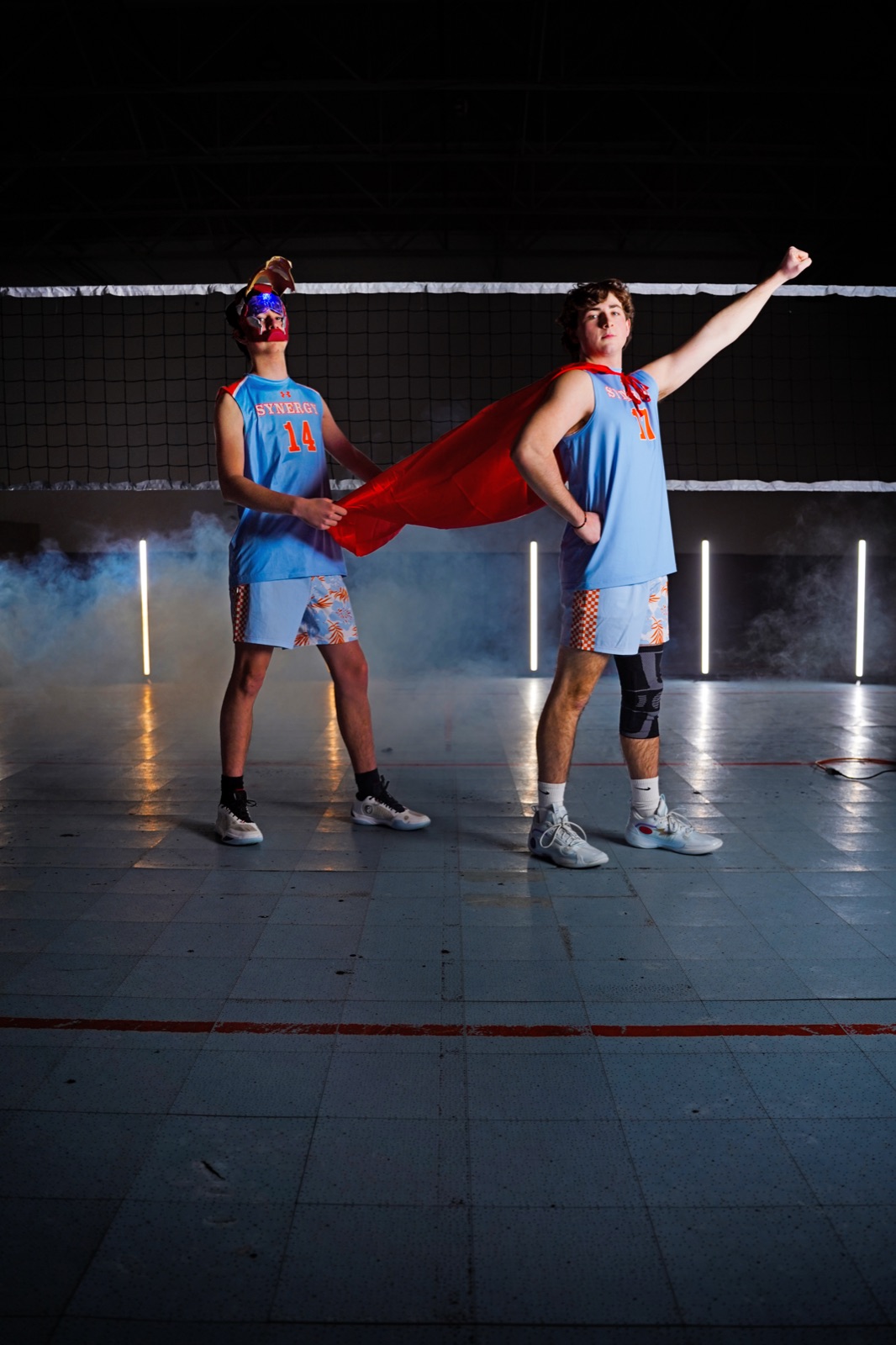 Two athletes clowning around — one wearing a superhero cape striking a pose